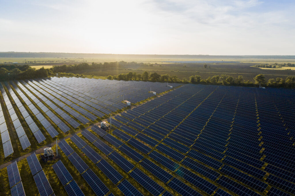 Luftaufnahme eines Solarparks auf verpachteten Freiflächen, der nachhaltige Energie produziert, mit klarem Himmel im Hintergrund